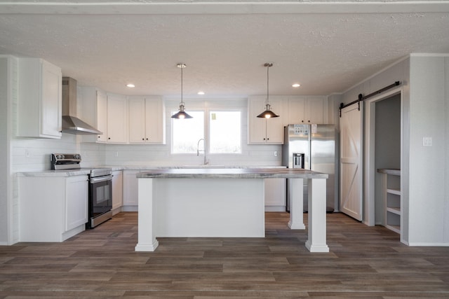 kitchen featuring a barn door, appliances with stainless steel finishes, wall chimney range hood, and white cabinetry