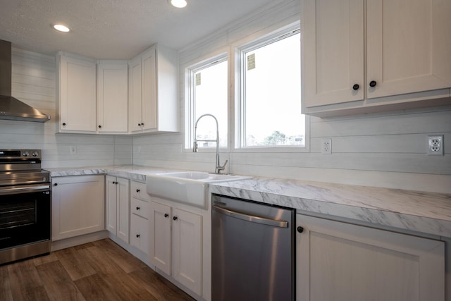kitchen with dark wood-style floors, a sink, stainless steel appliances, wall chimney exhaust hood, and light countertops