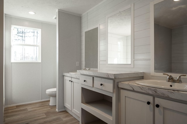 bathroom with a textured ceiling, a sink, two vanities, toilet, and wood finished floors