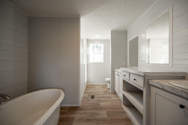 full bathroom featuring a textured ceiling, toilet, a freestanding tub, wood finished floors, and vanity