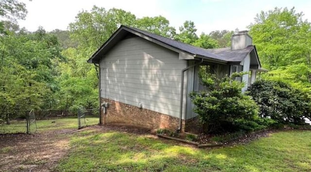 view of property exterior featuring fence, a chimney, a yard, and a forest view