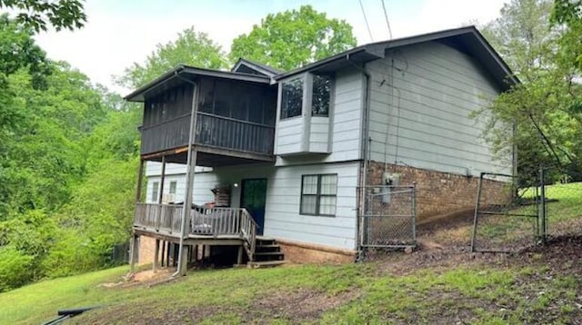back of house with a wooden deck, a gate, fence, brick siding, and a sunroom