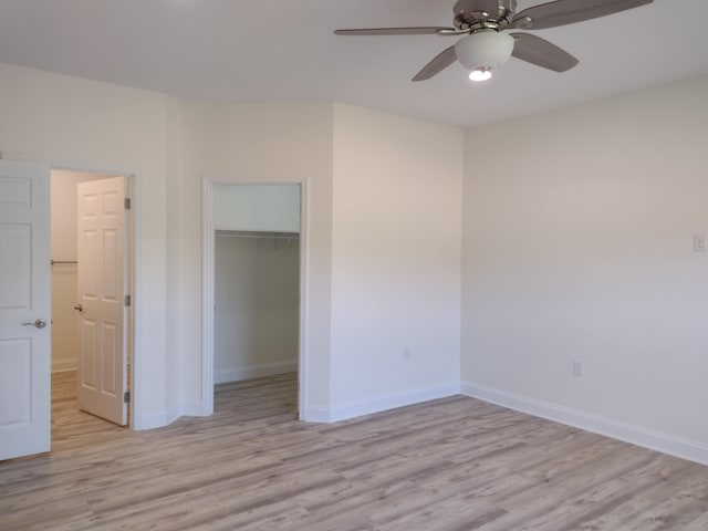 unfurnished bedroom featuring a closet, baseboards, a walk in closet, and light wood-style floors