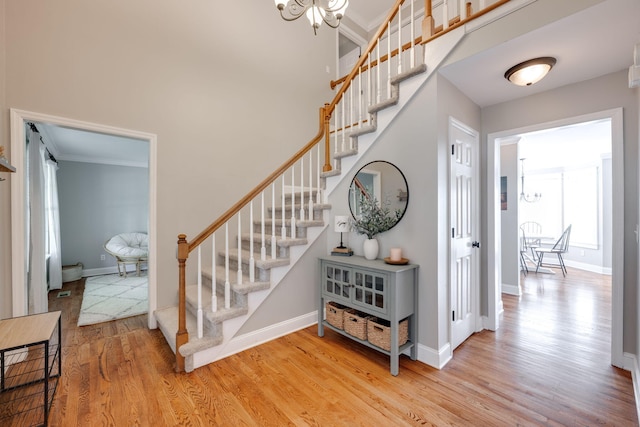stairway with baseboards, a notable chandelier, ornamental molding, and wood finished floors
