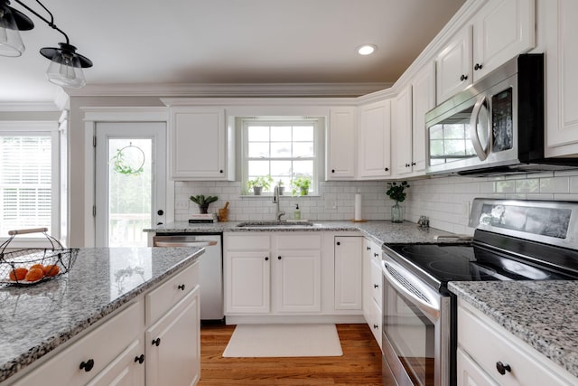 kitchen featuring ornamental molding, light wood finished floors, a sink, stainless steel appliances, and white cabinets