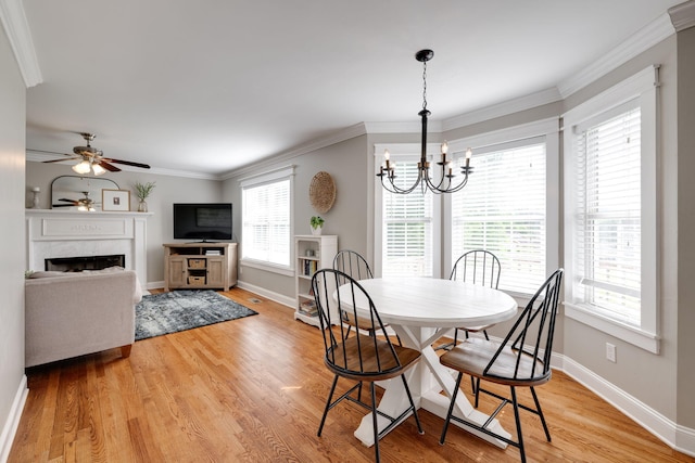 dining area with baseboards, ornamental molding, light wood finished floors, ceiling fan with notable chandelier, and a high end fireplace