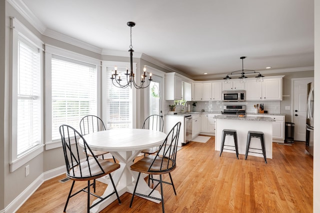 dining space featuring light wood finished floors, ornamental molding, a notable chandelier, and baseboards