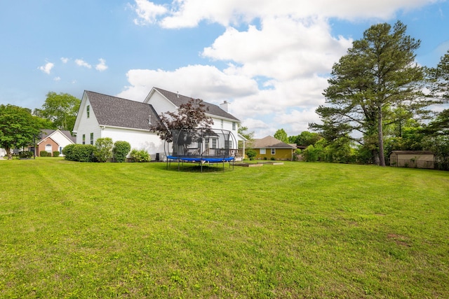 rear view of house featuring a trampoline, a shingled roof, and a lawn