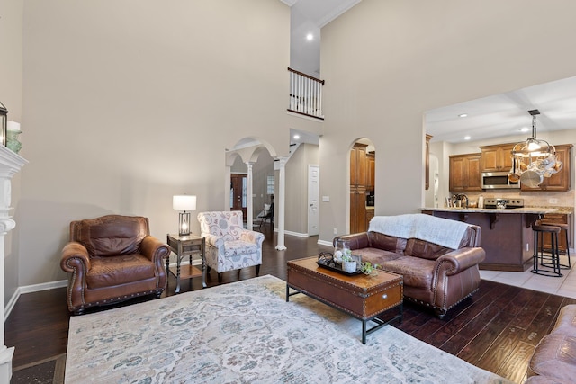 living room featuring crown molding, baseboards, arched walkways, decorative columns, and wood finished floors