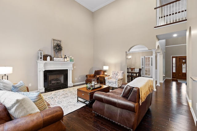 living area featuring hardwood / wood-style flooring, a towering ceiling, baseboards, arched walkways, and ornate columns