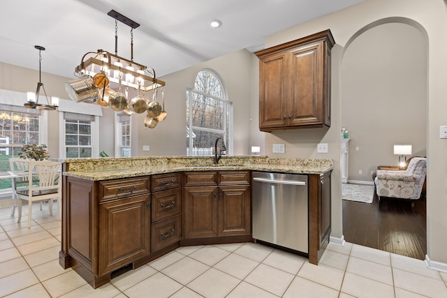 kitchen with a sink, light stone countertops, dishwasher, a peninsula, and a notable chandelier