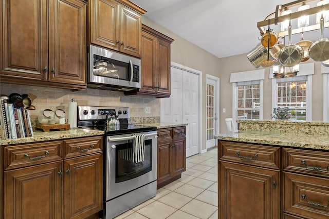 kitchen with light stone counters, tasteful backsplash, stainless steel appliances, an inviting chandelier, and light tile patterned flooring