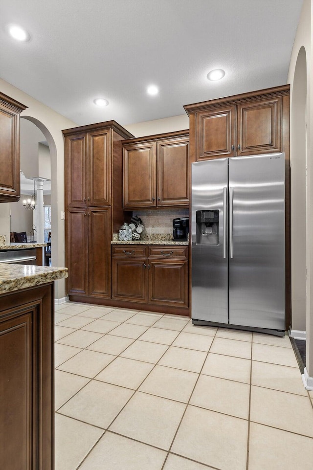 kitchen featuring light stone counters, stainless steel refrigerator with ice dispenser, light tile patterned flooring, and arched walkways