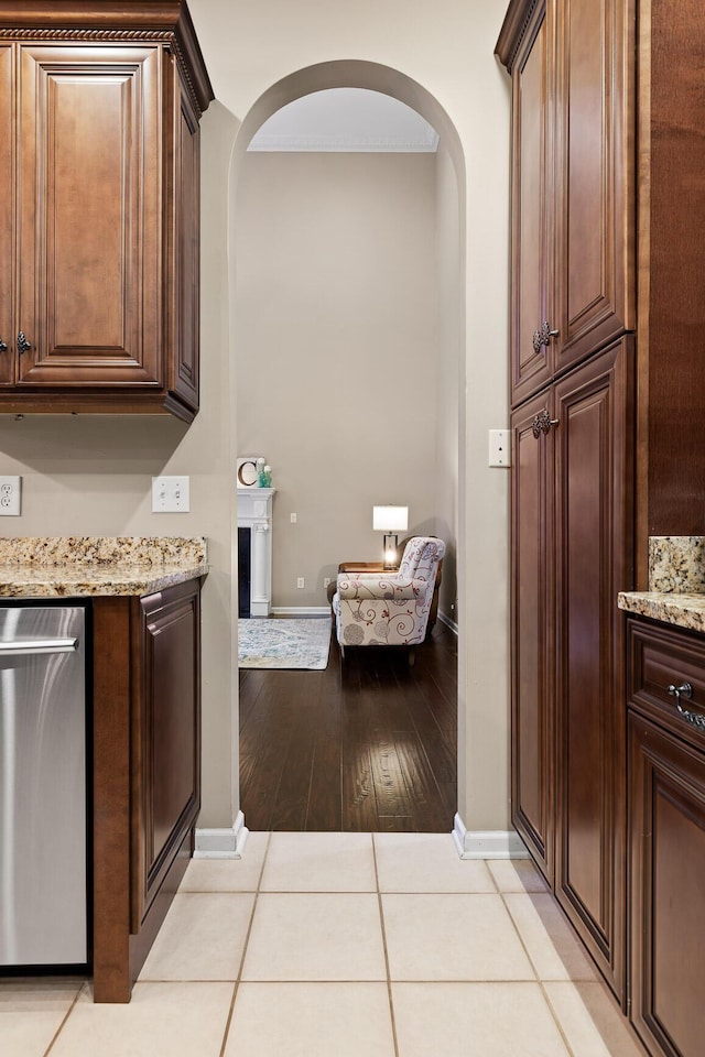 interior space featuring light stone counters, light wood-style flooring, dark brown cabinets, baseboards, and arched walkways