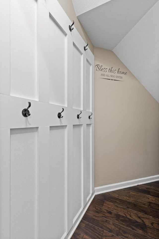 interior space featuring lofted ceiling, dark wood-type flooring, and baseboards