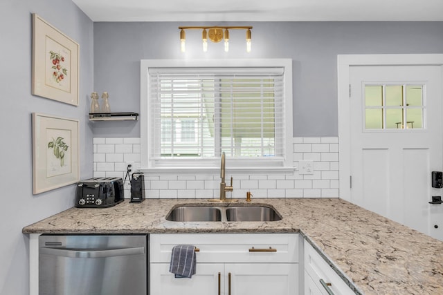 kitchen featuring stainless steel dishwasher, a sink, backsplash, and white cabinetry