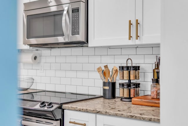 kitchen with stainless steel microwave, range with electric cooktop, light stone counters, backsplash, and white cabinets
