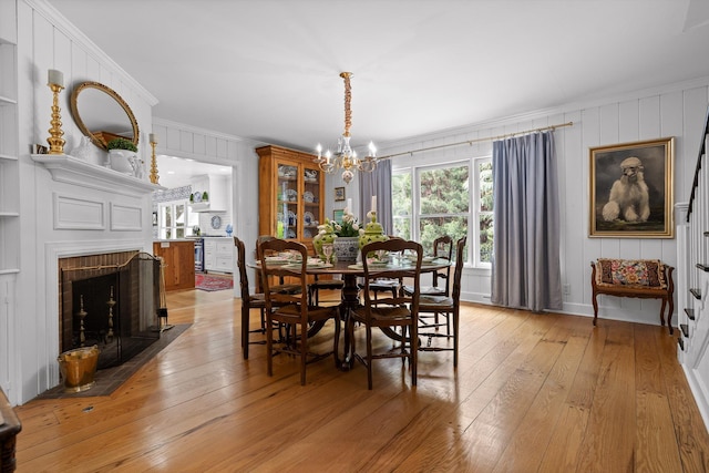 dining space with a brick fireplace, an inviting chandelier, ornamental molding, and light wood finished floors