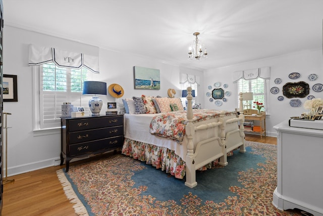 bedroom featuring baseboards, ornamental molding, wood finished floors, and a notable chandelier