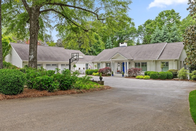 ranch-style house featuring curved driveway, an attached garage, roof with shingles, and a chimney