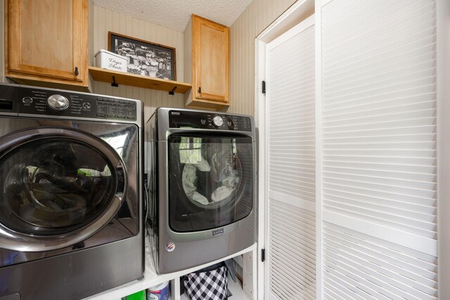 laundry area with cabinet space, a textured ceiling, and washing machine and dryer