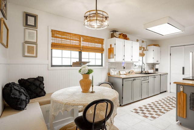 kitchen featuring hanging light fixtures, wainscoting, a sink, light countertops, and stainless steel dishwasher