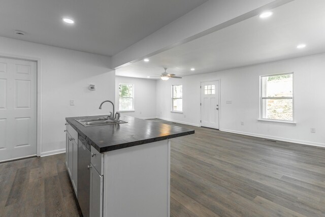 kitchen featuring a ceiling fan, baseboards, a sink, an island with sink, and dark wood-style floors