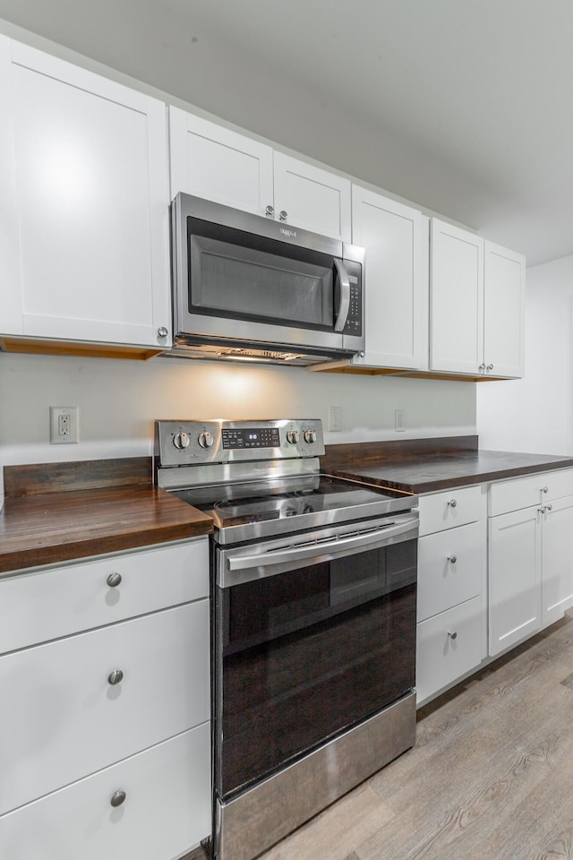kitchen with wood counters, light wood-style floors, stainless steel appliances, and white cabinetry