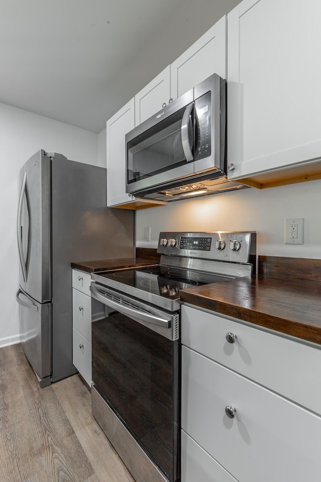 kitchen with wood counters, light wood-type flooring, stainless steel appliances, and white cabinetry