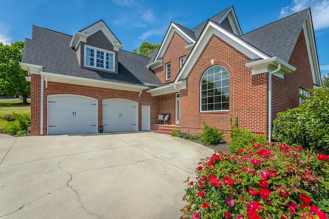traditional-style home featuring a shingled roof, an attached garage, concrete driveway, and brick siding