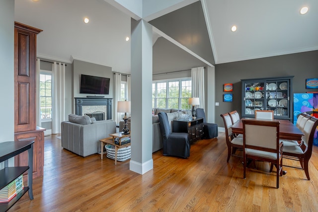 dining area featuring ornamental molding, lofted ceiling, a fireplace, baseboards, and light wood-style flooring