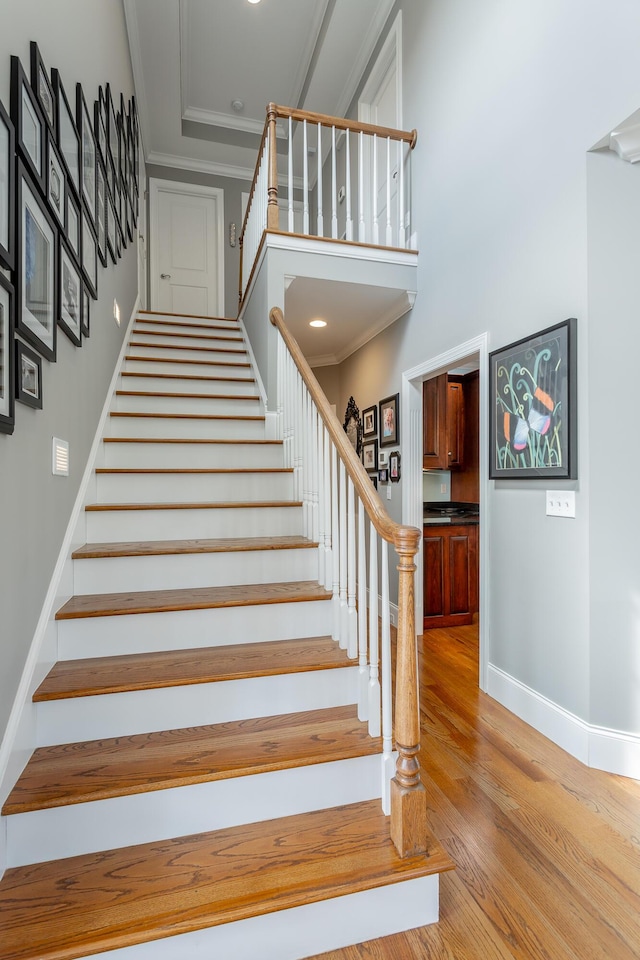 stairs featuring crown molding, wood finished floors, baseboards, a high ceiling, and recessed lighting