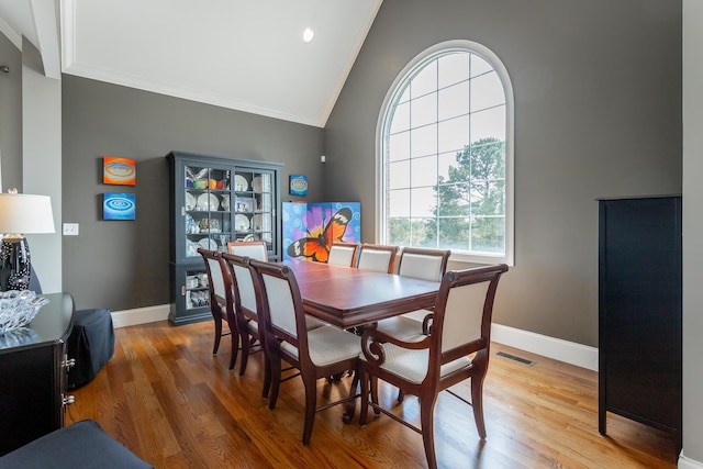 dining room with visible vents, crown molding, baseboards, lofted ceiling, and light wood-style flooring