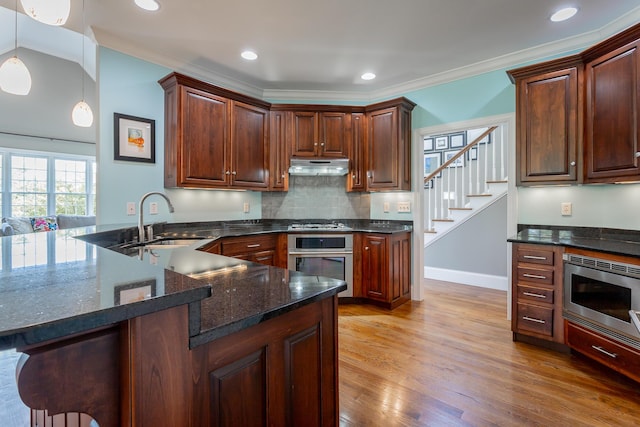 kitchen with backsplash, a sink, dark stone countertops, light wood finished floors, and stainless steel appliances