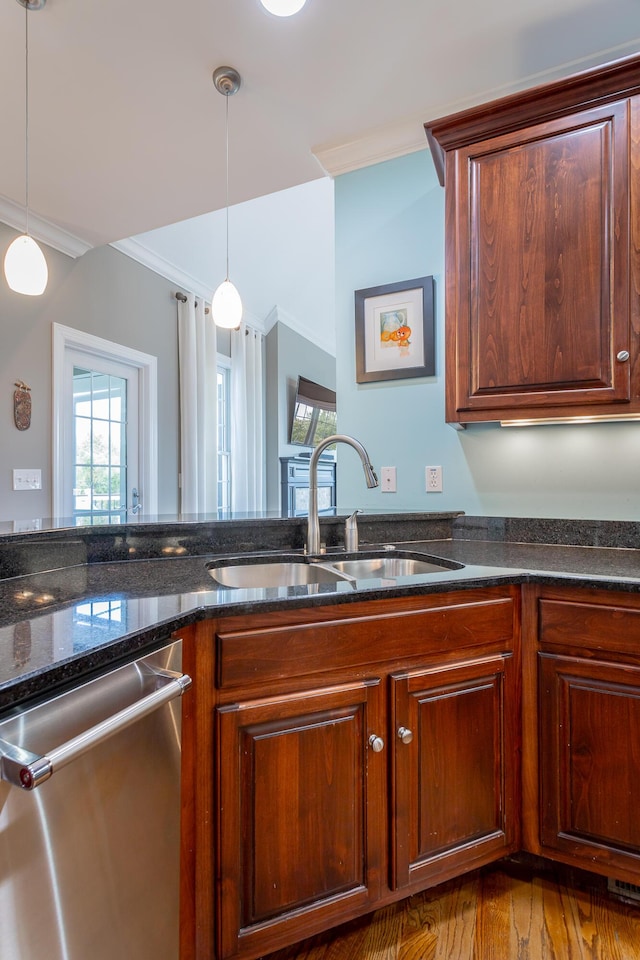 kitchen featuring stainless steel dishwasher, crown molding, a sink, dark stone countertops, and hanging light fixtures