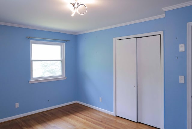 unfurnished bedroom featuring baseboards, ornamental molding, light wood-style flooring, and a closet