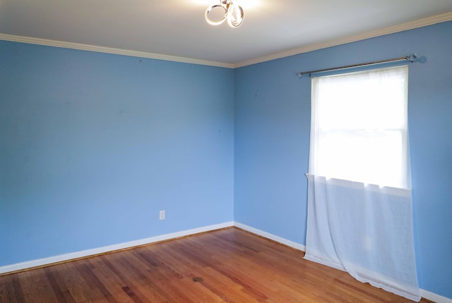 spare room featuring crown molding, baseboards, wood finished floors, and a notable chandelier