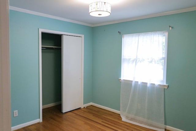 unfurnished bedroom featuring baseboards, ornamental molding, wood finished floors, and a closet