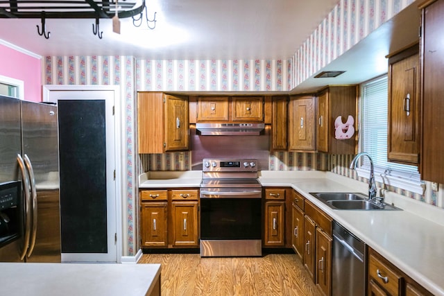 kitchen with wallpapered walls, light countertops, under cabinet range hood, a sink, and stainless steel appliances