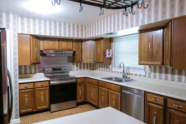 kitchen featuring brown cabinets, a sink, under cabinet range hood, stainless steel appliances, and wallpapered walls