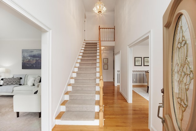 staircase with an inviting chandelier, baseboards, wood finished floors, and a towering ceiling