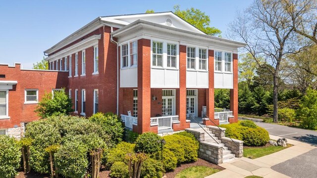 view of front of property featuring covered porch, brick siding, and french doors