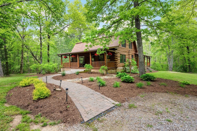 log-style house featuring roof with shingles, log exterior, a porch, and a front lawn