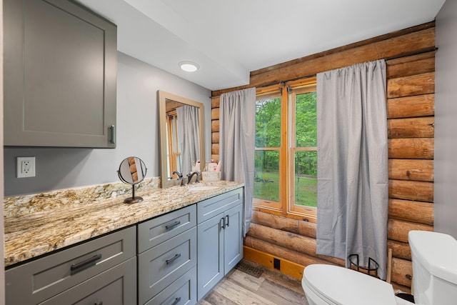 bathroom with vanity, rustic walls, wood finished floors, and toilet
