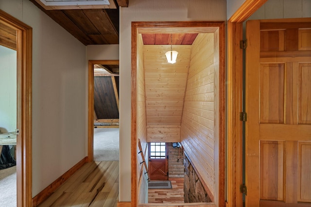 hallway featuring wooden walls, baseboards, wooden ceiling, and wood finished floors