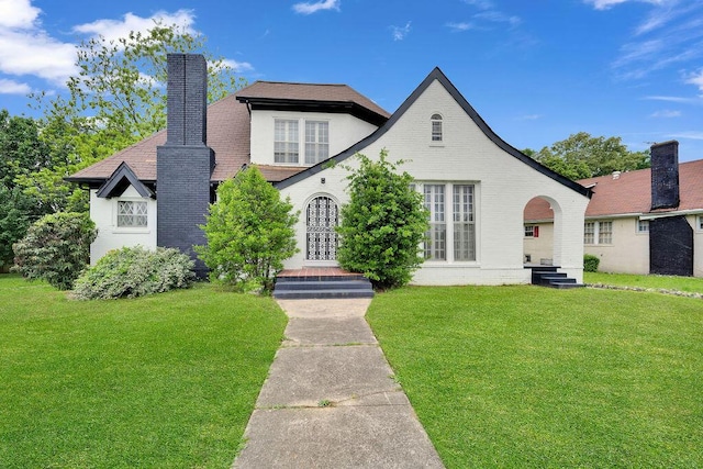 tudor house featuring a chimney, a front lawn, and brick siding