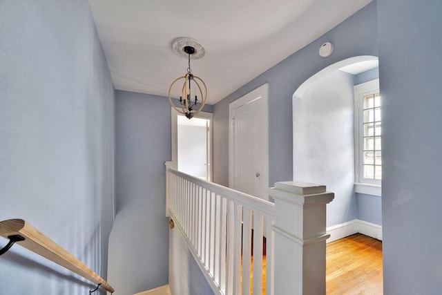 corridor featuring baseboards, an upstairs landing, wood finished floors, arched walkways, and a chandelier