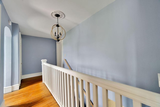 hall featuring wood finished floors, a chandelier, baseboards, and an upstairs landing