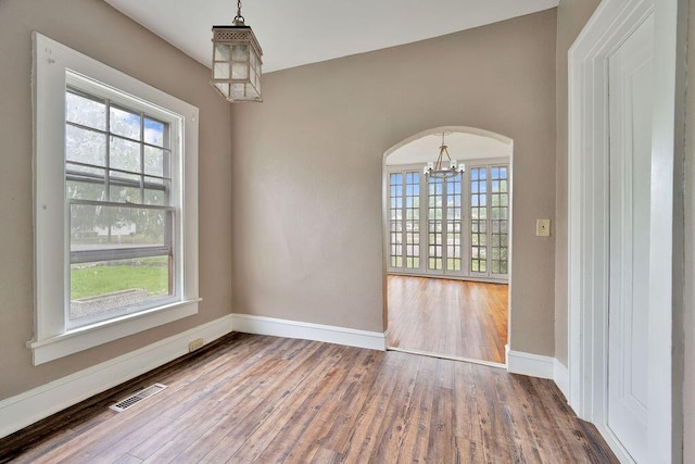 empty room featuring a chandelier, wood finished floors, baseboards, and arched walkways