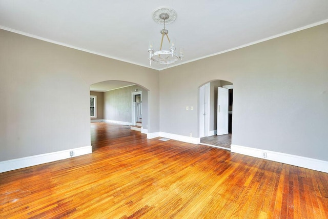 unfurnished room with arched walkways, hardwood / wood-style flooring, baseboards, a chandelier, and crown molding